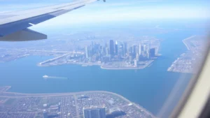 Aerial view of Boston skyline with harbor and downtown skyscrapers visible from airplane window during daytime flight approach