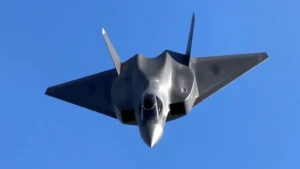 Modern stealth fighter jet in flight against blue sky, sleek aerodynamic design with angular surfaces, photographed from below showing advanced aircraft technology