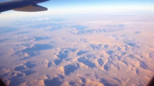 Aerial view from commercial aircraft window showing desert landscape with mountains and valleys between Austin Texas and Las Vegas Nevada, bright daylight with wing visible