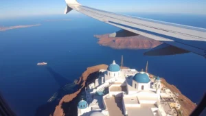 Santorini caldera view from airplane window during descent, white-washed buildings and blue domes visible below, morning sunlight, photorealistic travel photography