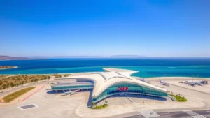 Aerial view of Olbia Costa Smeralda Airport terminal with Mediterranean Sea in background, modern architecture, clear sunny day