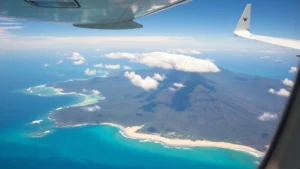 Aerial photograph of Hawaii islands showing turquoise ocean waters, white sand beaches, and lush green volcanic terrain from aircraft window during daytime descent to Honolulu with scattered clouds