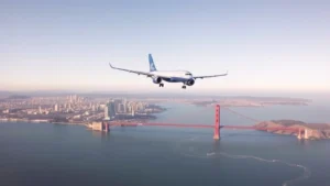 Aerial view of San Francisco Bay with Golden Gate Bridge visible, modern city skyline in background, daytime clear weather, commercial airplane in flight approaching the bay