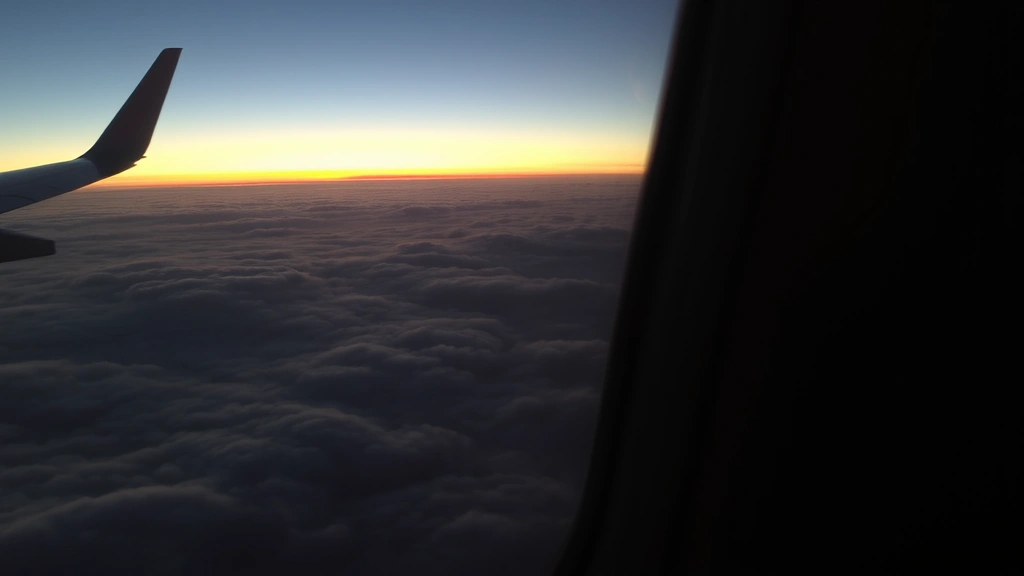 Window seat view of sunset over clouds at high altitude during evening flight, wing visible with landing lights, distant horizon showing earth curvature, peaceful in-flight atmosphere