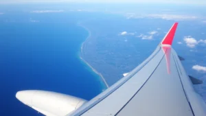 Commercial airplane wing in flight over Pacific Ocean with California coastline visible below during daytime