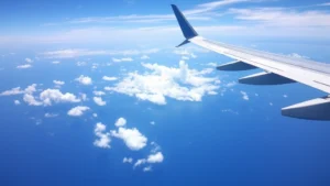 Aerial view of a commercial aircraft flying over the Pacific Ocean toward distant Hawaiian islands with blue ocean and white clouds below, bright daylight conditions