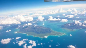 Aerial view of Hawaiian islands from cruising altitude, Pacific Ocean turquoise waters visible below, white clouds scattered across landscape, daytime golden light